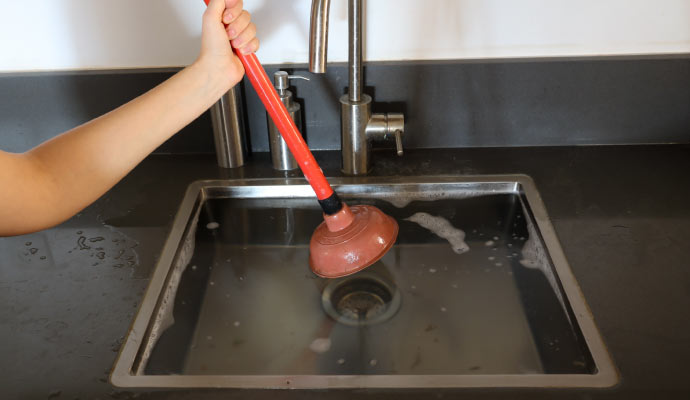 Someone is using a plunger to try and clear a blockage in a sink full of soapy water